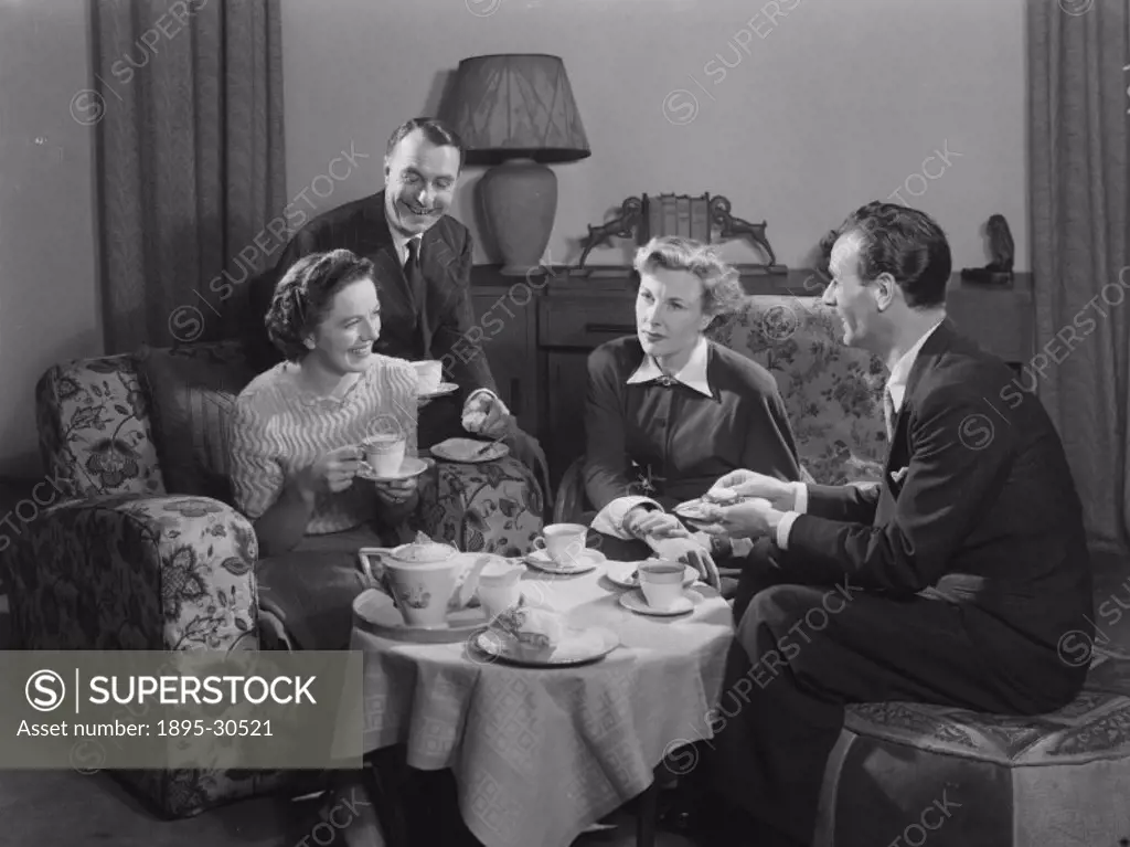 A photograph of two couples having a pot of tea and cakes together in their living room, taken by Photographic Advertising Limited in 1949.  This imag...