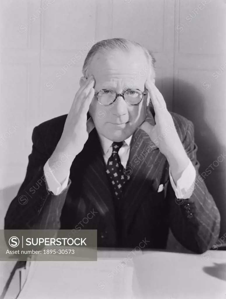 A photograph of a middle-aged man dressed in a business suit, holding his head in his hands, taken by Photographic Advertising Limited in 1958.  Photo...
