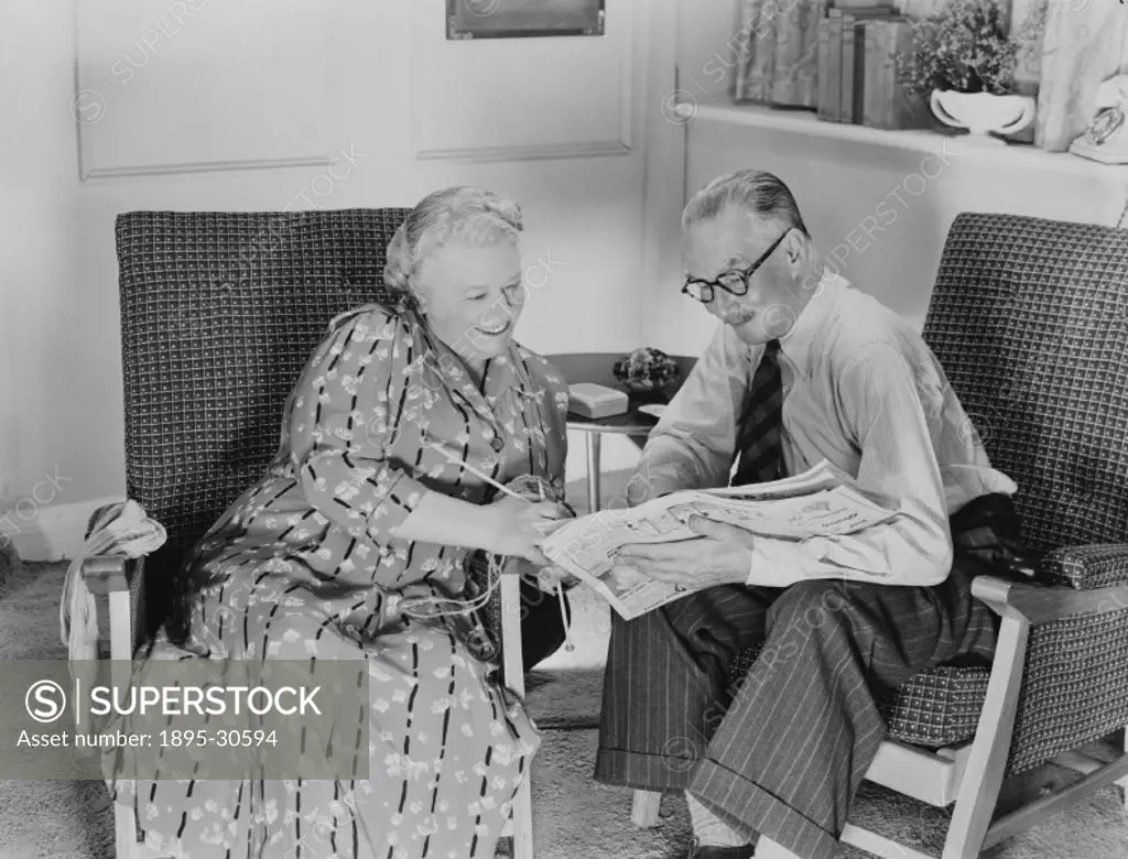 A photograph of an elderly couple sitting in armchairs, reading the newspaper together, taken by Photographic Advertising Limited in 1950.  Photograph...