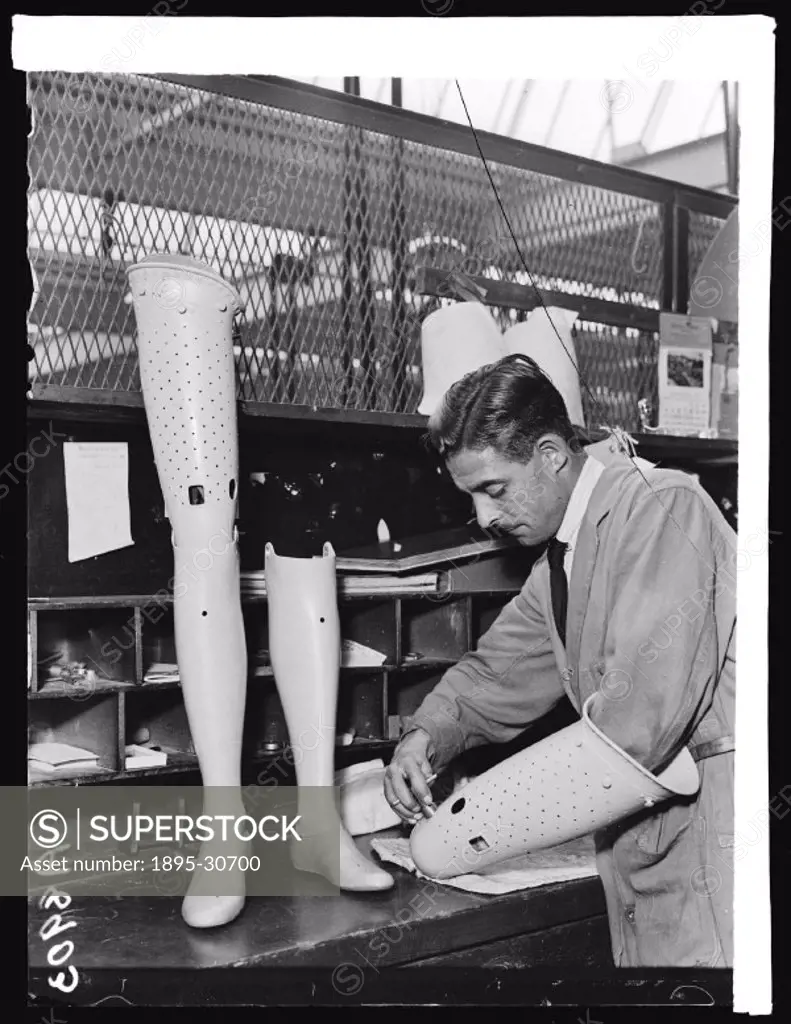 A photograph of a man assembling a pair of artificial legs at Desoutter Brothers´ artificial limbs factory at Hendon, taken by Harold Tomlin for the D...