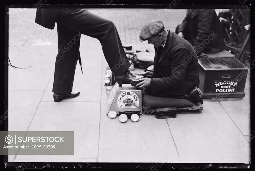 A photograph of a man kneeling to polish someone´s shoes, taken by Woodbine for the Daily Herald newspaper on 12 October, 1932.   The shoeshiner is su...