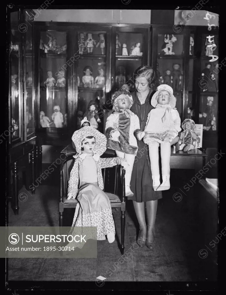 A photograph of a woman with three large rag dolls, taken by Cardew for the Daily Herald newspaper on 26 October, 1932.  These rag dolls had soft clot...