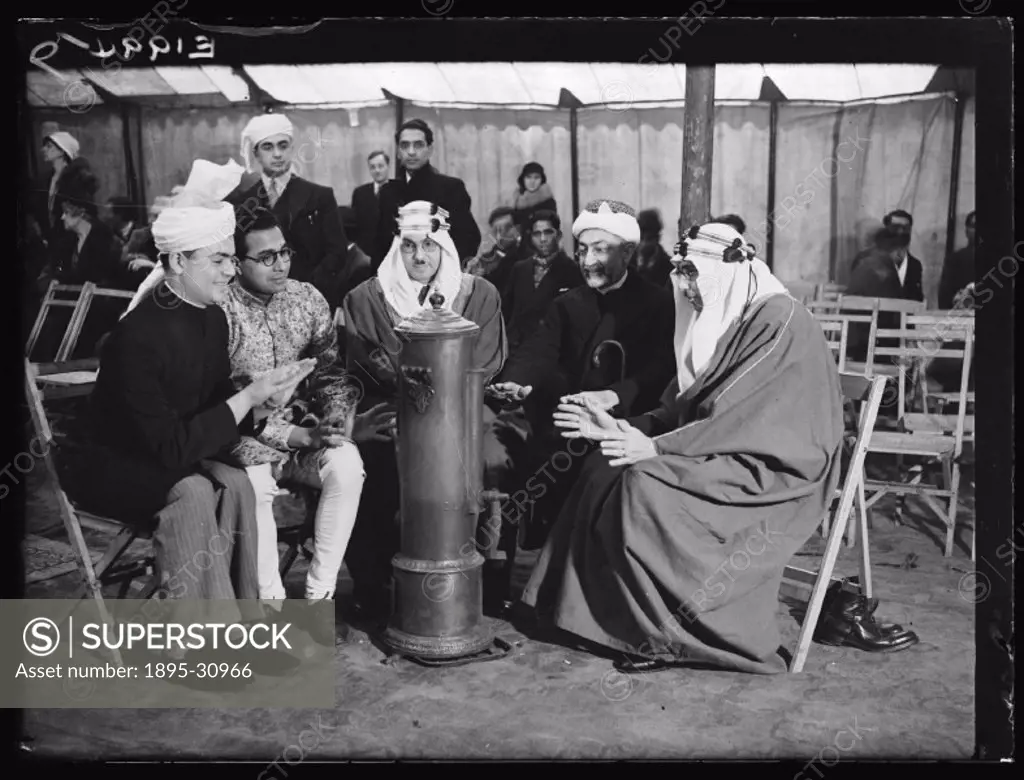 A photograph of a group of Muslim leaders warming themselves around a heater at the Shah Jehan Mosque in Woking, Surrey, taken by Malindine for the Da...