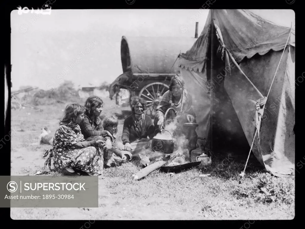 A photograph of a Romany family sitting around a cooking fire in an encampment, taken by Tomlin for the Daily Herald newspaper on 3 June, 1935. This f...