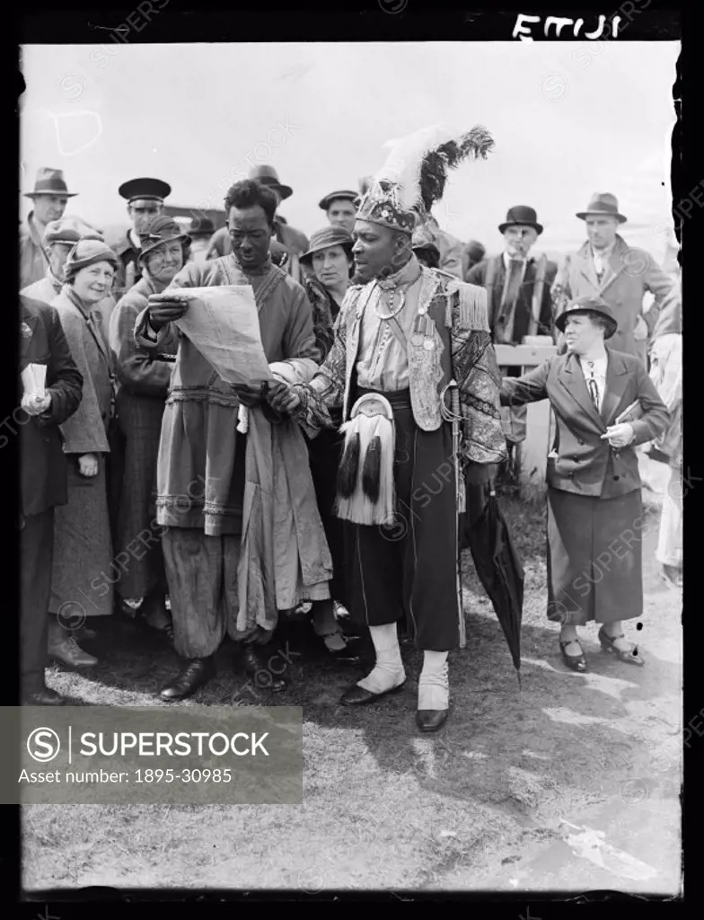 A photograph of two exotically-dressed men reading out horse racing tips at Epsom racecourse, taken by Malindine for the Daily Herald newspaper. Crowd...
