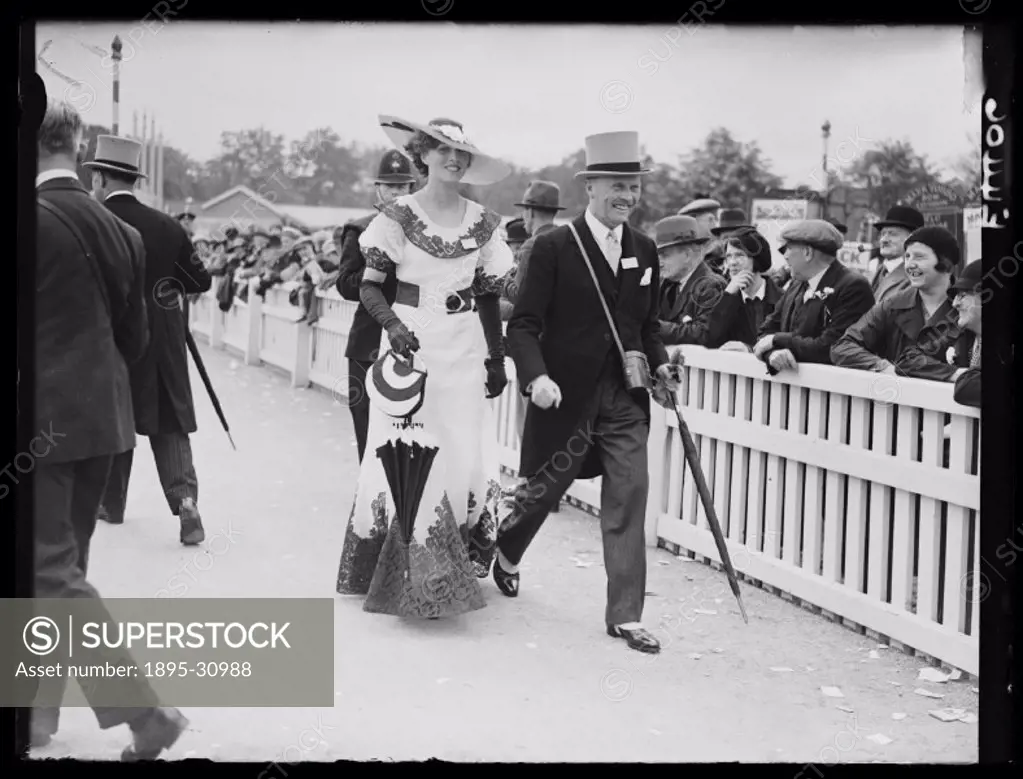 A photograph of a couple walking past racegoers on the second day of Royal Ascot for the Royal Hunt Cup horse-race, taken by Edward Malindine for the ...
