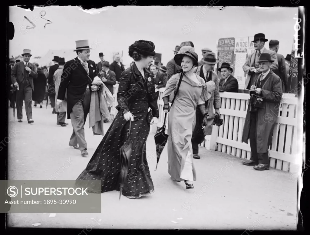 A photograph of two women walking through the crowds on the second day of Royal Ascot for the Royal Hunt Cup horse-race, taken by Edward Malindine for...
