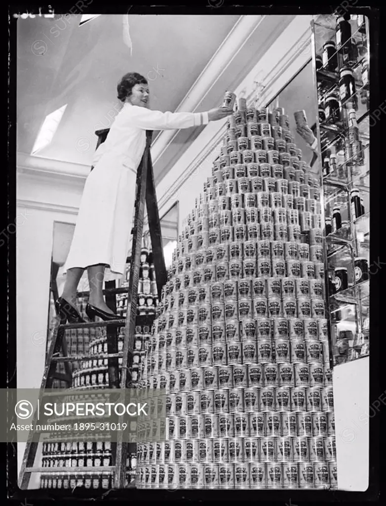 A woman climbs a ladder to assemble a giant display of Heinz baked beans with pork.