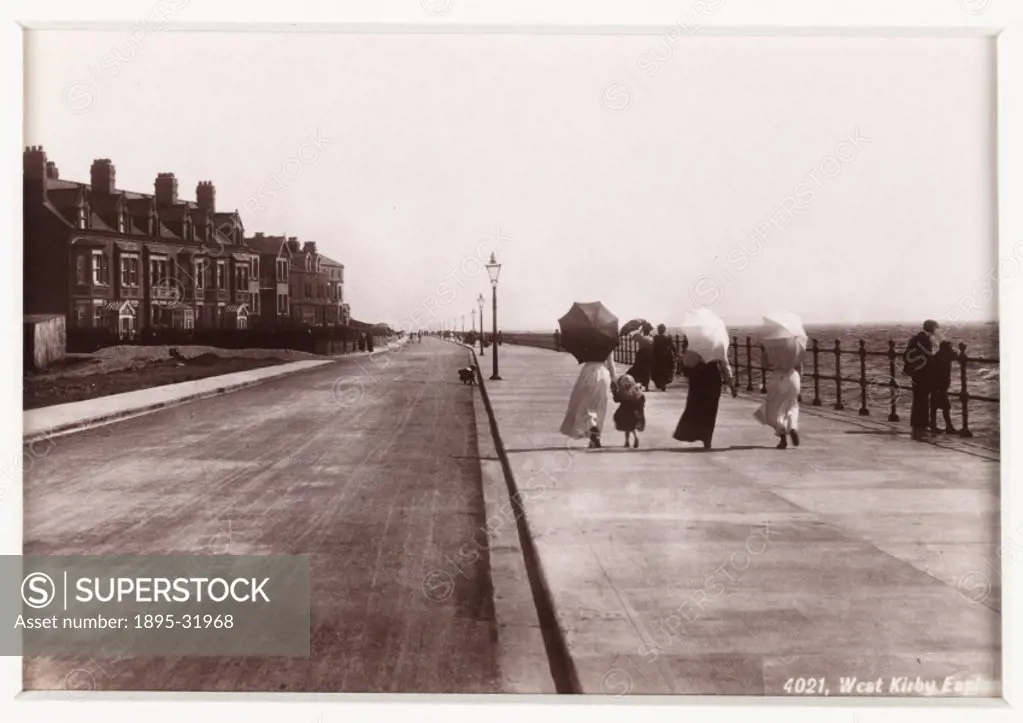 A photographic view of three women and a child with parasols strolling along the Esplanade in West Kirby on what looks like a windy day, published by ...