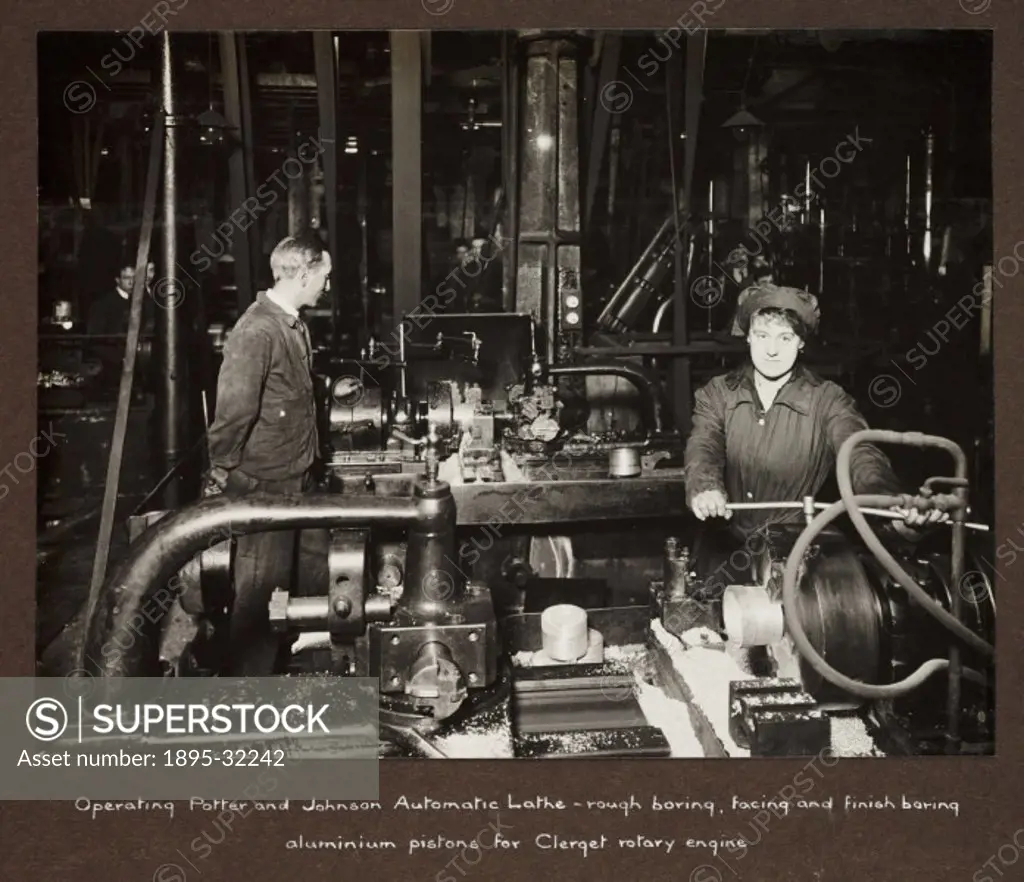 A photograph taken by an unknown photographer during 1915-1918 of a woman operating a machine lathe in a British factory.  A male supervisor stands ne...