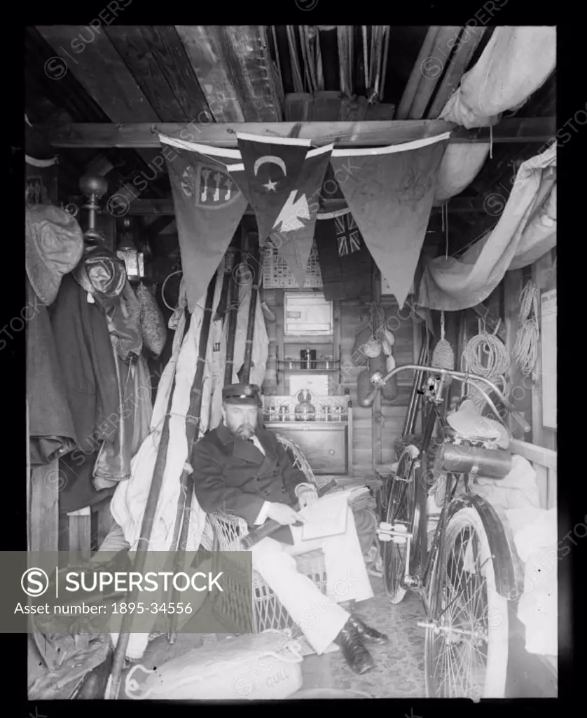 A photograph of Edgar Tarry Adams (1852-1926), dressed for sailing and carrying a telescope, sitting in his boathouse in Deal, Kent, possibly taken by...