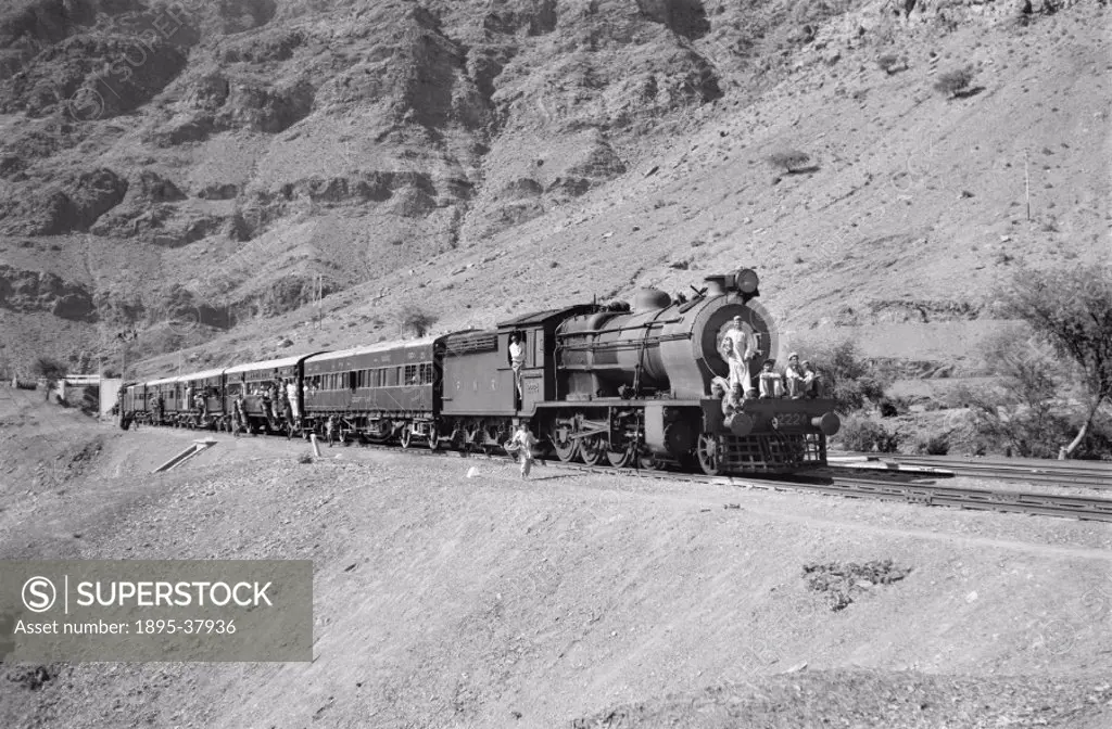 Passenger train, pulled by a steam locomotive at Shahgai, Pakistan, by Peter Bawcutt, 1968. This line, on the Khyber railway, runs through a very moun...