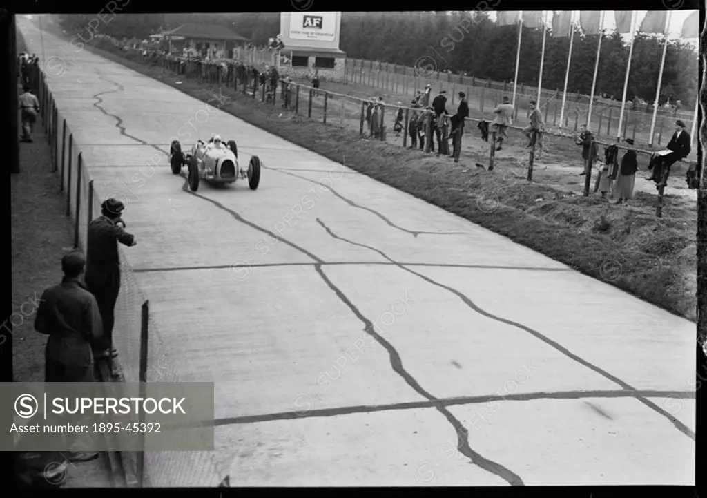 Photograph by Zoltan Glass. Spectators beside the track watch Stuck in his Auto-Union A-Type V16 at the back of the pits.