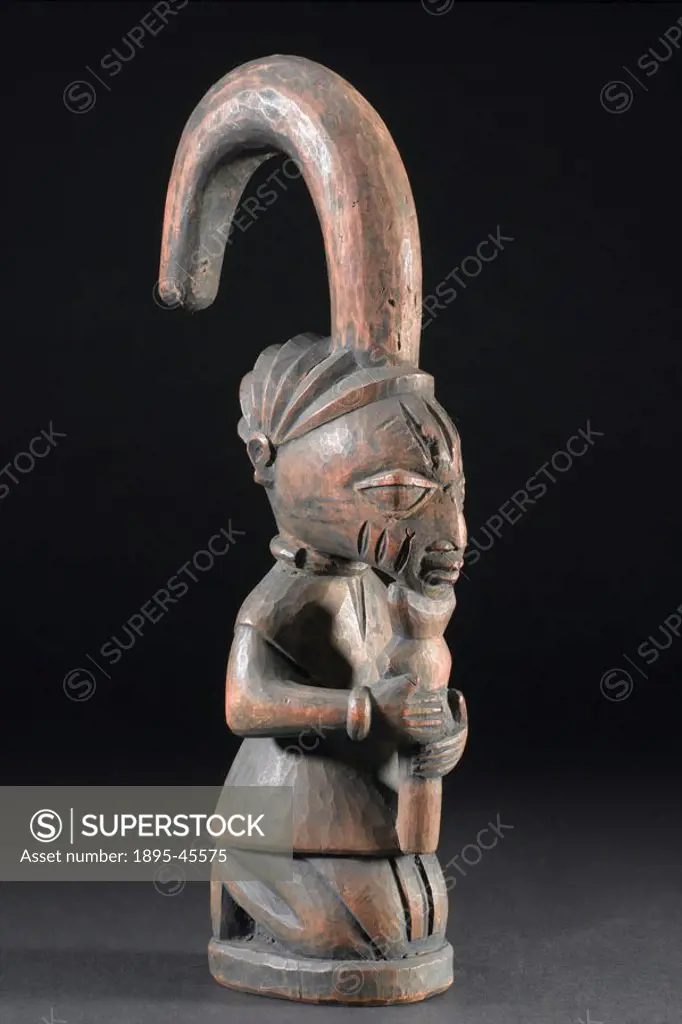 Carved figure of Eshu/Elegba kneeling and holding a notched stuck under its chin, with backward-curving hooked headdress, made by the Yoruba people, W...