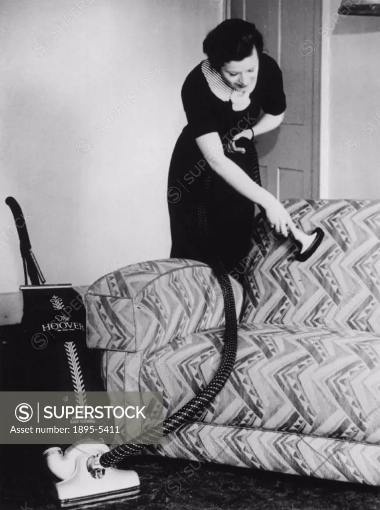 A woman cleaning her settee using the latest Hoover vacuum cleaner.