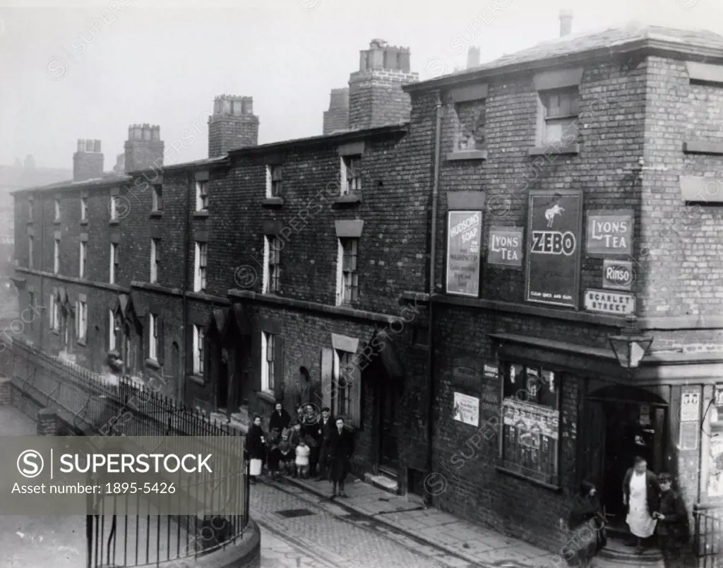 Photograph by Edward Malindine showing a the exteriors of slum properties in Scarlet Street, Liverpool. Outside one f the houses is a group of people ...