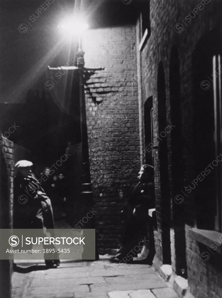 Men loitering in the street at night in a slum area of London, 1937.