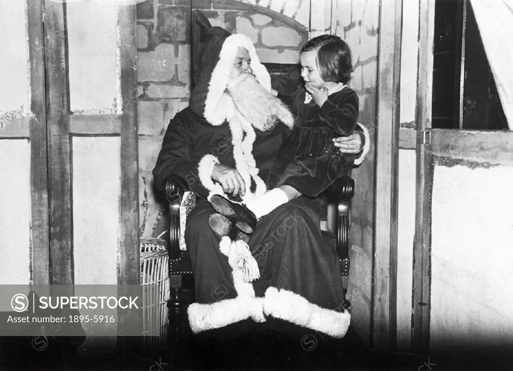 Father Christmas at Pontings of Kensington´s department store, London. ´His little visitor is interested in his bag of toys´.