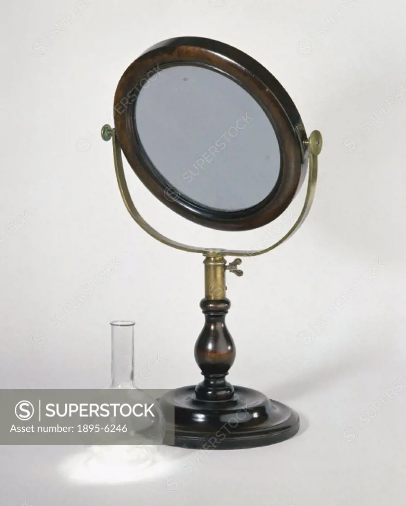Heat is produced as sunlight is focused by a large convex lens, such as this example which is mounted on a brass pivot on a wooden stand. Heat can cau...