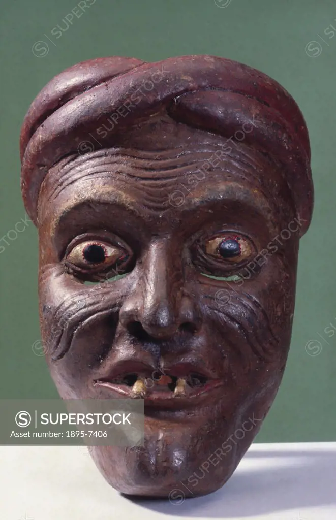 This wooden mask shows a brown-faced, gap-toothed, wrinkled man wearing a turban, possibly a peasant from the kolam masked play, and was worn for heal...