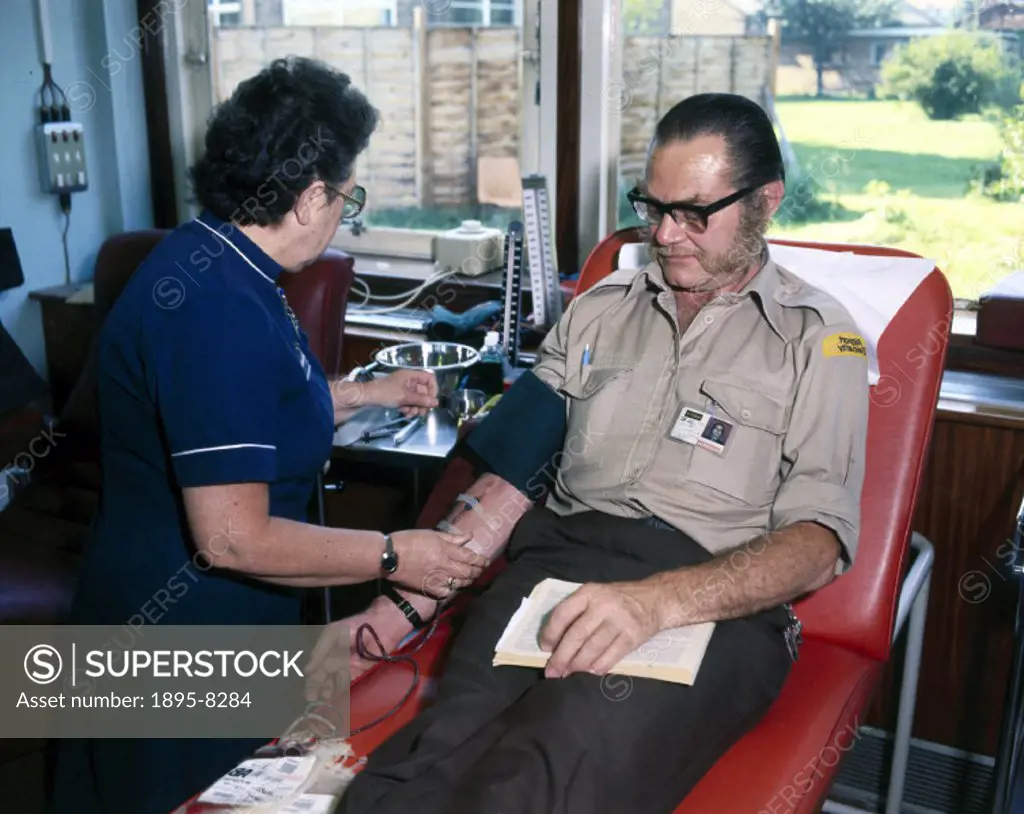 A man giving blood at the North London Blood Transfusion Centre, being attended to by a nurse.