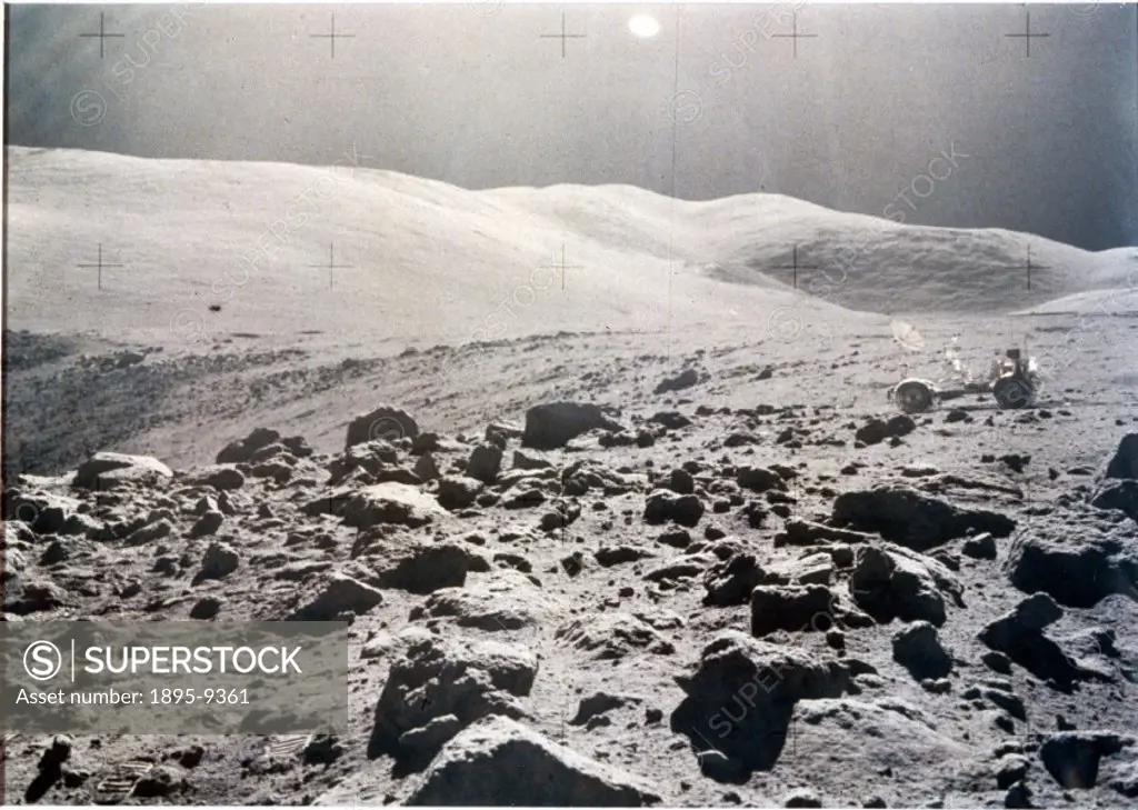 This view shows a rock-strewn landscape with rolling hills in the background. The Lunar Rover vehicle can be seen in the distance. Apollo 15, the four...