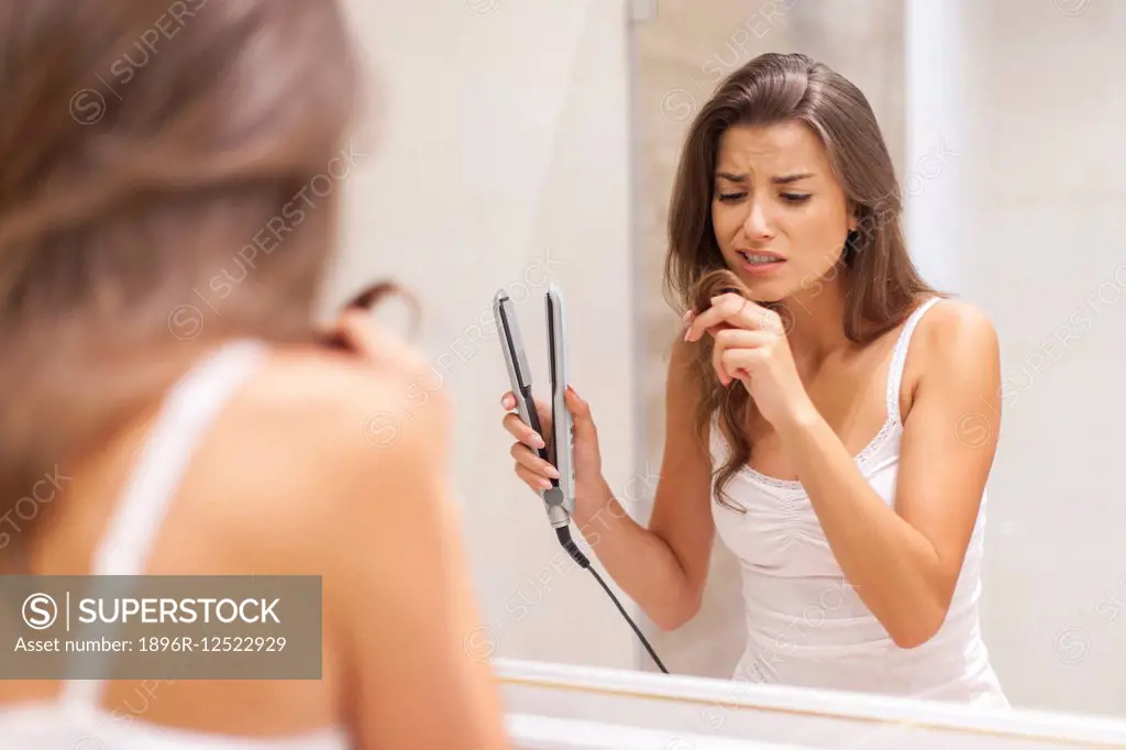 Woman straightening hair in bathroom. Debica, Poland