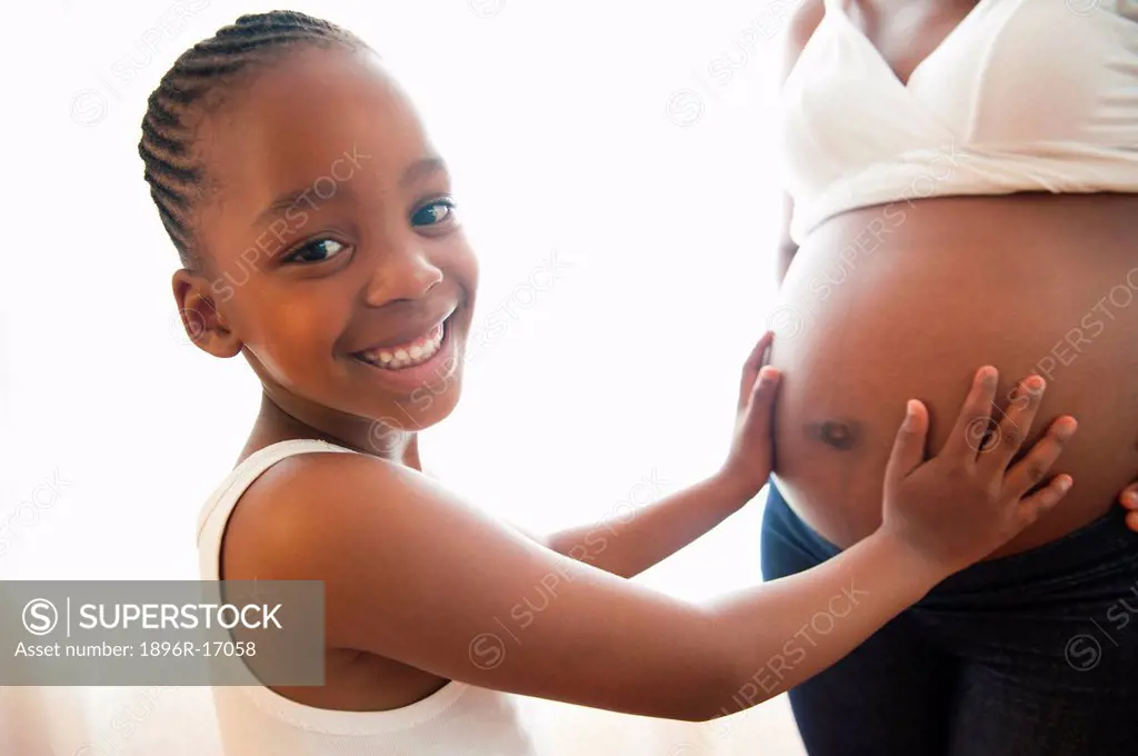 Portrait of young girl with hands on pregnant mother´s stomach, Johannesburg, Gauteng Province, South Africa
