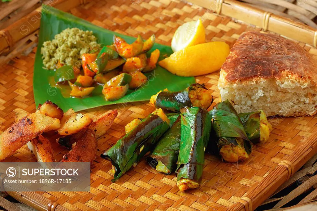Indian cooking. Baked fish in banana leaves served with golden potatoes, coconut chutney, mango pickle and naan bread