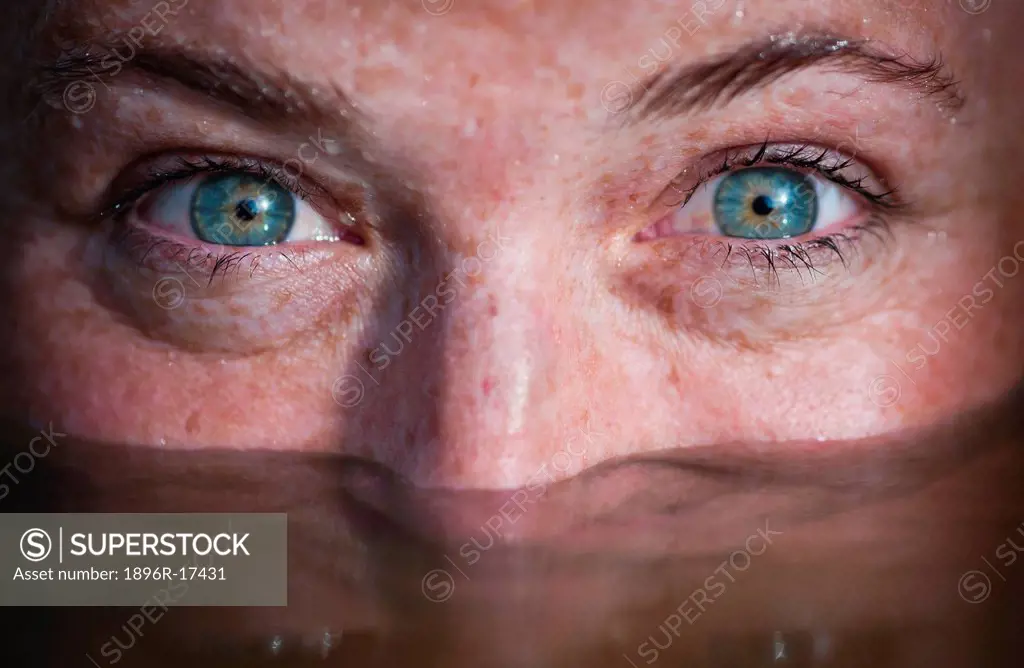 Close_up of woman´s face half submerged in water with only her eyes staring at camera in Pai, Northern Thailand, Thailand.
