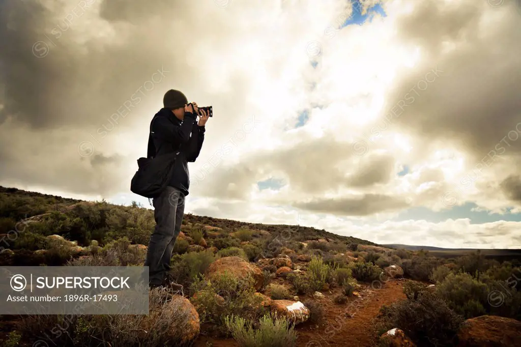 Young photographer aiming his camera to take a shot with beautiful nature scenery and dramatic sky in the background, Sutherland, Great Karoo, Groot K...