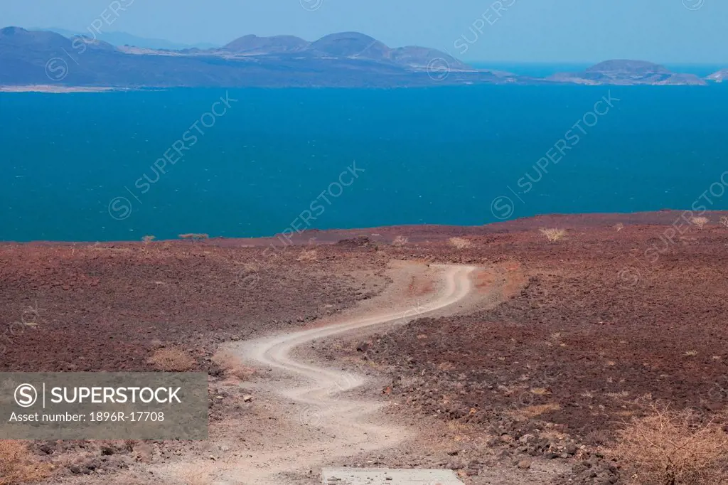 Dirt track leading through volcanic rocks to Lake Turkana/ Jade Sea, Loyongalani region, Lake Turkana, Kenya, Africa