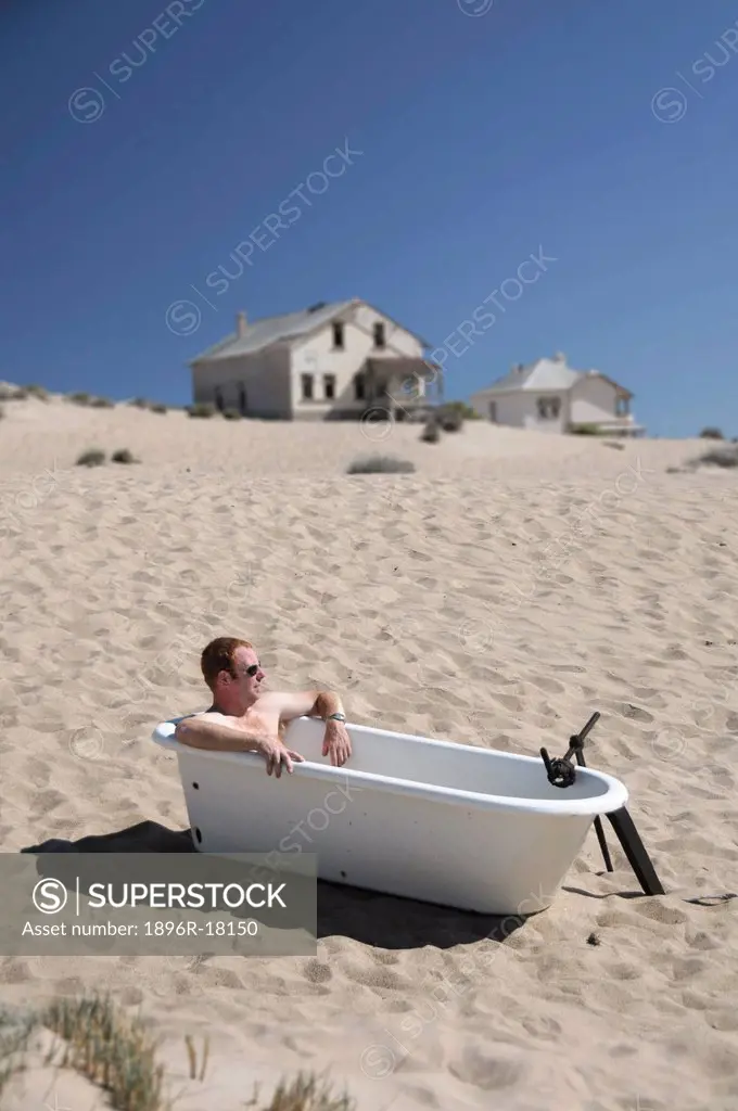 Man sitting in victorian bathtub on sand dune, Kolmanskop, Luderitz, Karas Region, Namibia