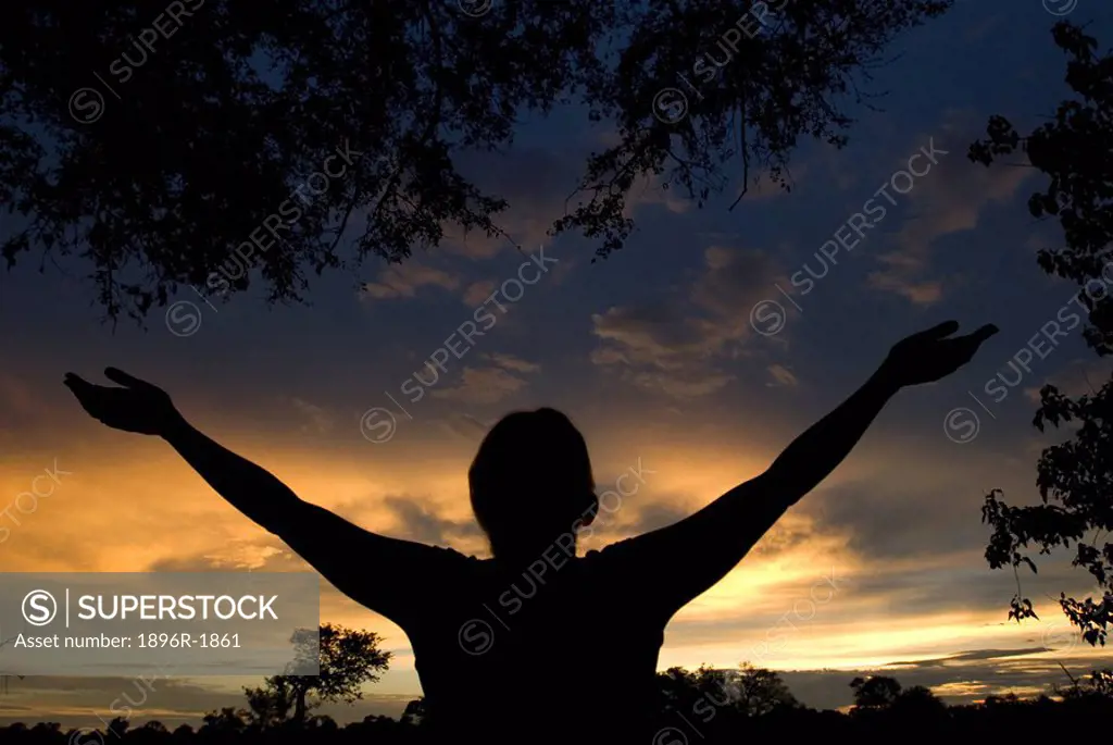 Silhouette of woman with her arms upraised at sunset, Moremi Wildlife Reserve, Botswana