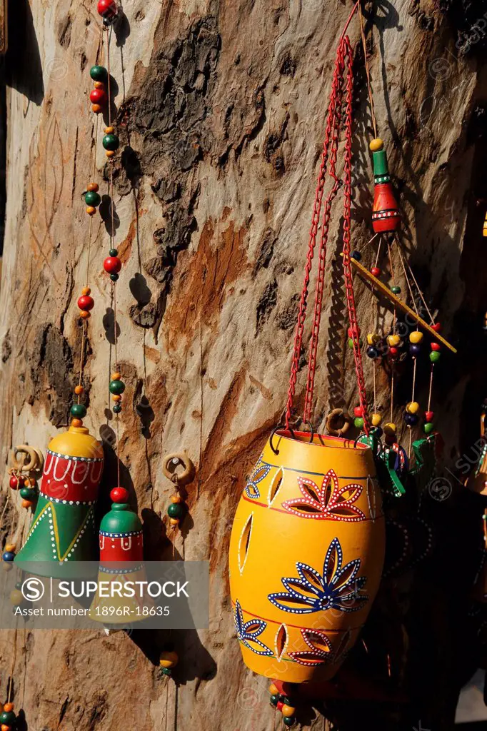 India, New Delhi. Dilli Haat crafts bazaar. Hand made and hand painted wooden wind chimes and bells displayed on a tree trunk.