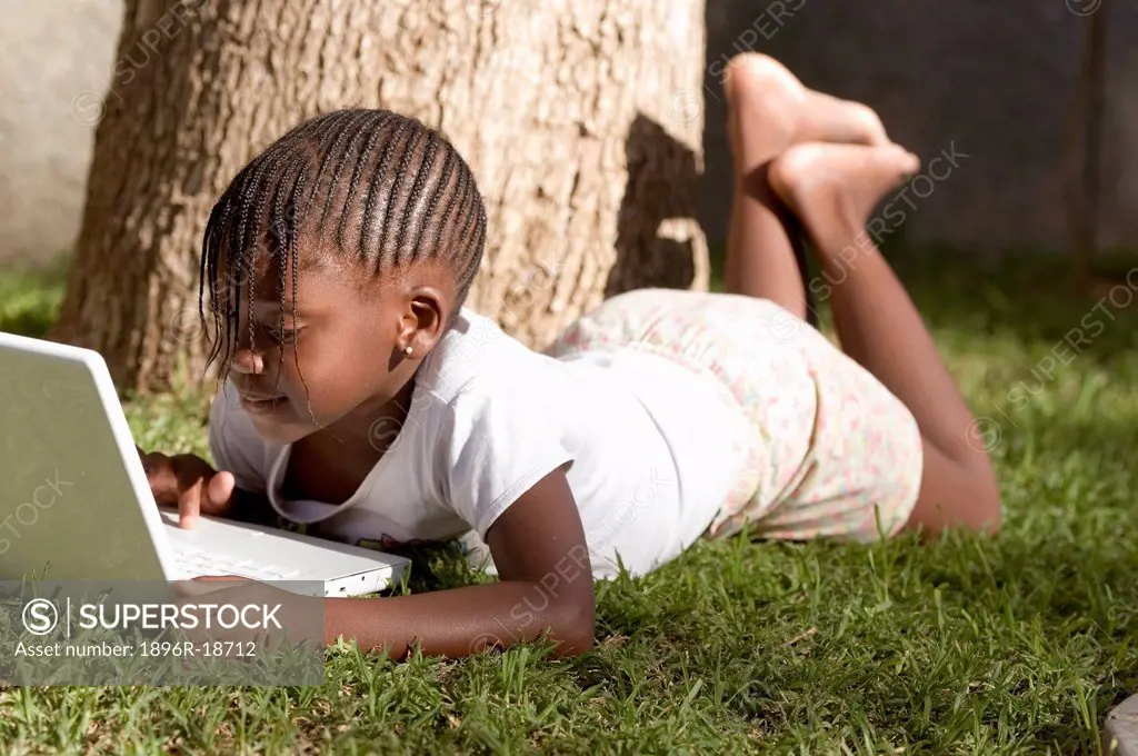 A young African girl lying in the grass working on computer. Windhoek, Namibia.