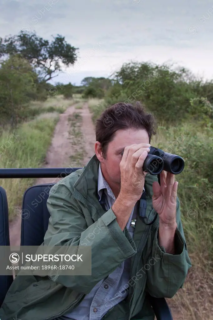 A visitor to the Sabie Sands Reserve, searches for wild life through his binoculars while travelling on a safari vehicle through the bushveld and sava...