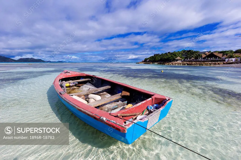 Wide angle view of a little fishing boat moored in shallow waters., turquoise water and the iconic granite rocks of Anse Source d'Argent beach. La Dig...