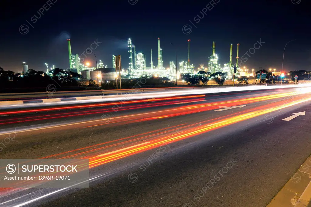 Wide angle view of traffic light streaks on a road with the lights and chimneys of an oil refinery in the background. Cape Town Chevron refinery, West...