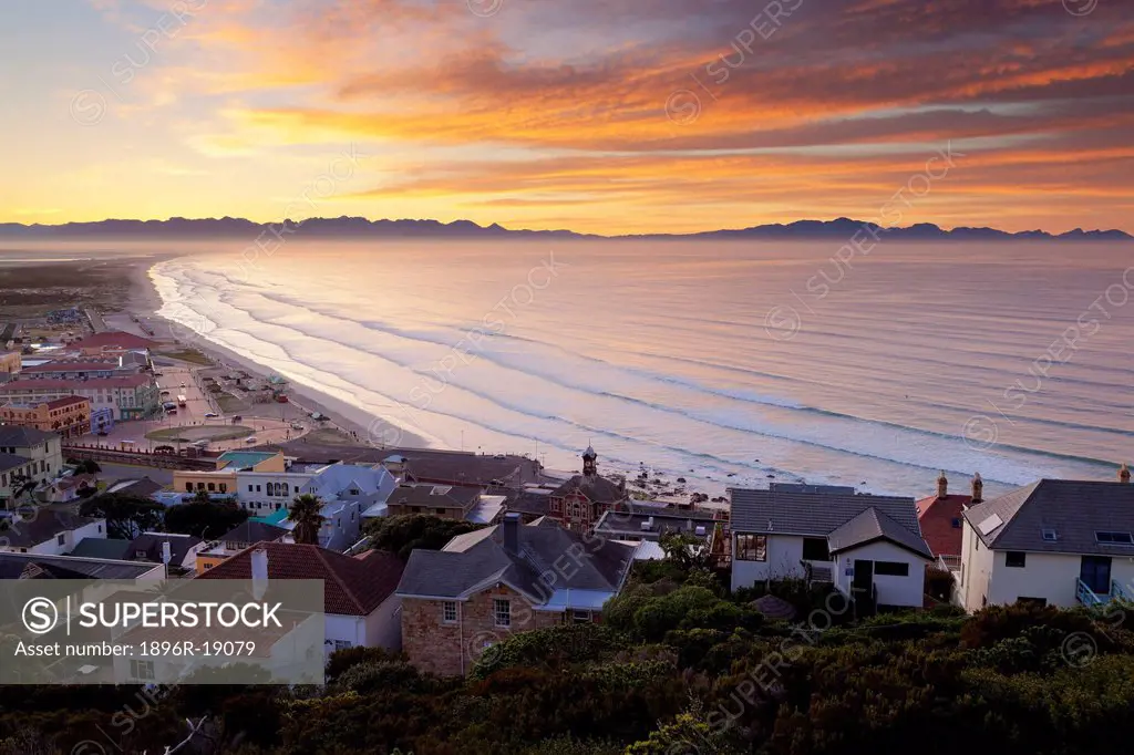 Wide view of a dramatic sunrise overlooking Muizenberg beach towards the Hottentots Holland mountains in the distance. False Bay, Western Cape, South ...