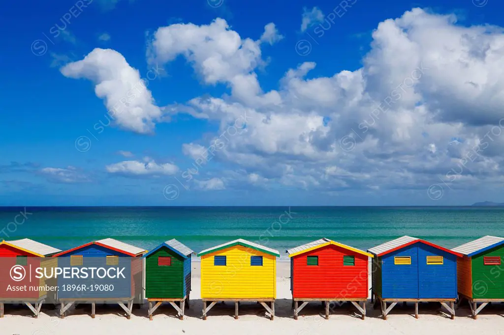 Wide view of the iconic Muizenberg beach huts under cloudy blue summer sky. Western Cape, South Africa