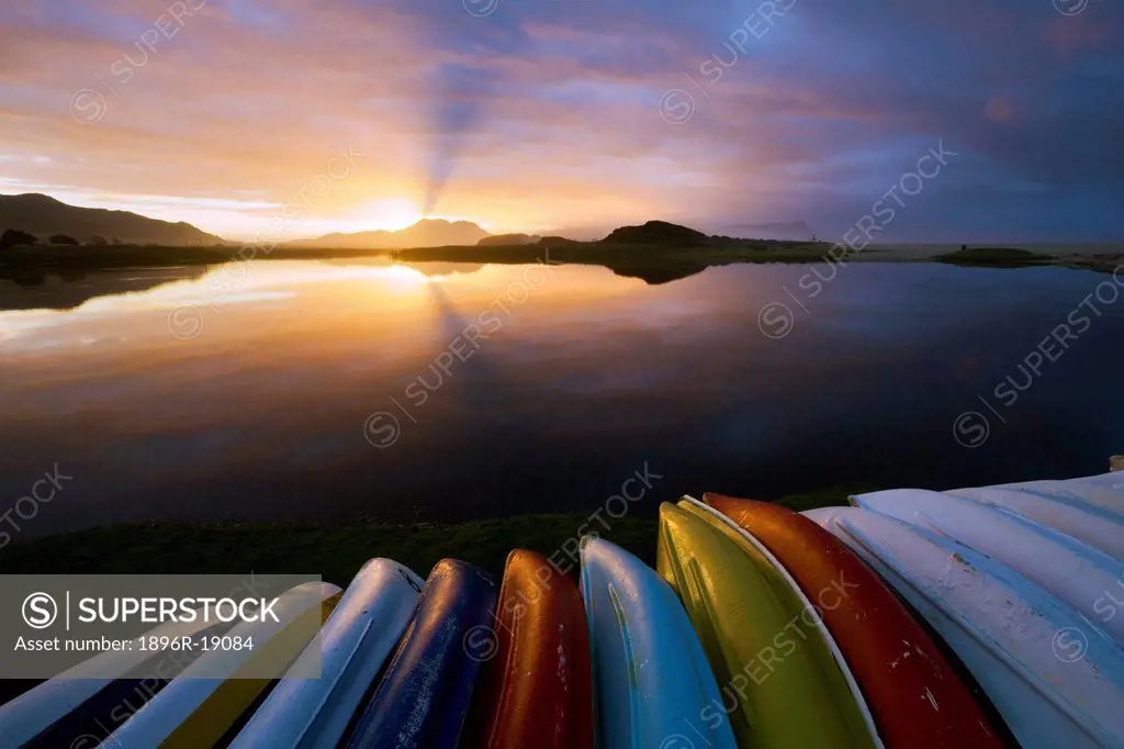 Wide angle view of a dramatic sunrise over a boats stacked along the edge of a lagoon. Kleinmond, Western Cape, South Africa