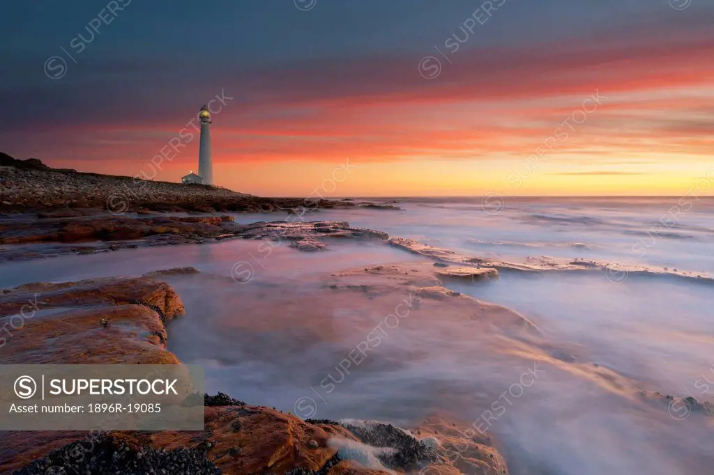 Wide angle view of a dramatic sunset over the Slangkop Lighthouse at Kommetjie. Cape Peninsula, Western Cape, South Africa