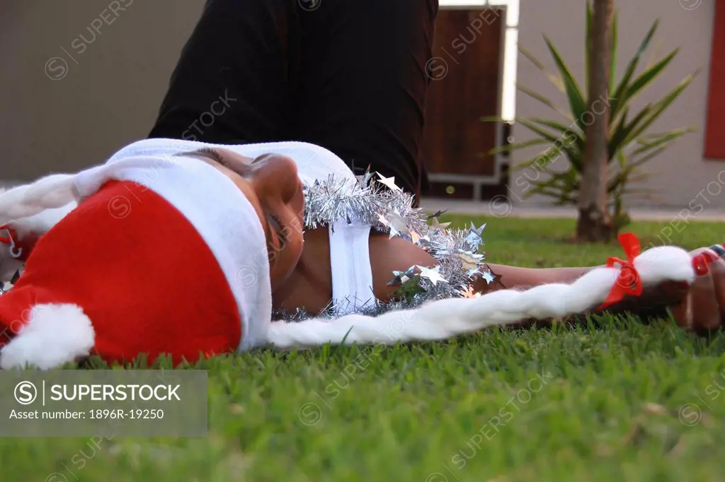 Young woman lying on her back on grass wearing santa hat and tinsel, Johannesburg, South Africa