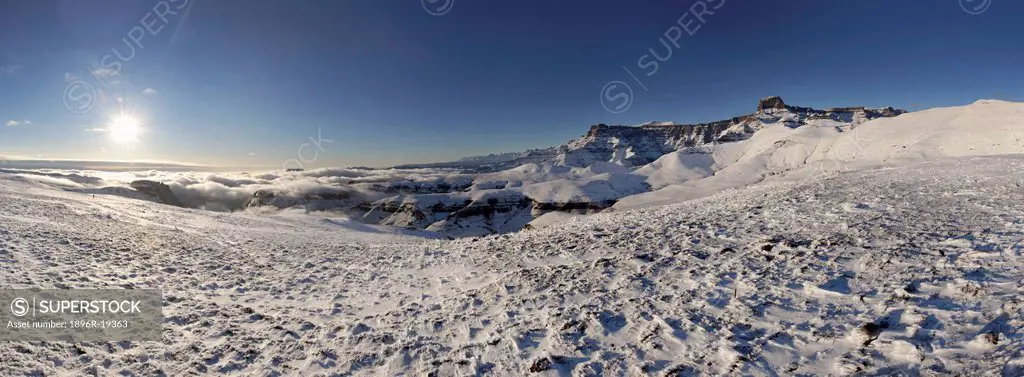 Panoramic view of sun rising over snow and ice on a slope with the Drakensberg Amphitheatre in the background, Witsieshoek, Free State Province, South...