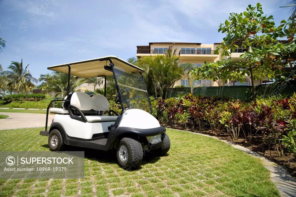 Golf cart on a carefully manicured lawn in front of a resort clubhouse in Mexico