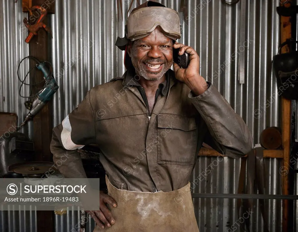 Metal worker using a mobile phone in his workshop. Philippi, Cape Town, South Africa.
