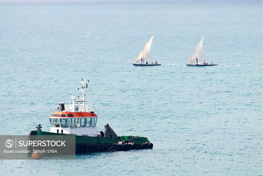 Tug boat with two mashua dhows in the background on a calm sea, Stone Town, Unguja Island, Zanzibar, Tanzania