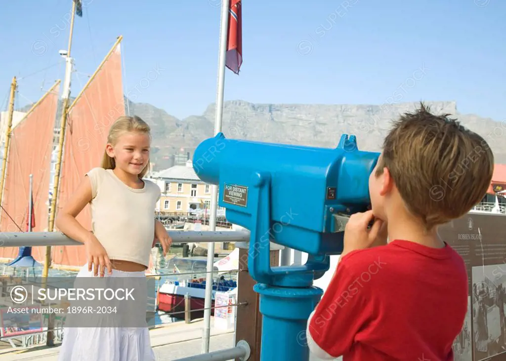 Boy looking at girl through telescope from Waterfont with Table Mountain in background, Cape Town, Western Cape Province, South Africa