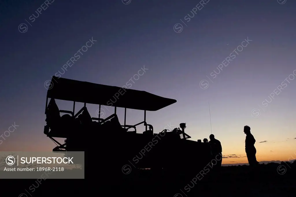 4x4 game viewer and tourists silhouetted at sunset, Okavango Delta, Botswana